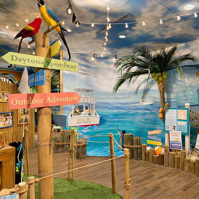 picture of an island-inspired bamboo walkway, rustic wooden signs pointing to daytona and hilton head with hanging string lights and ocean imagery
