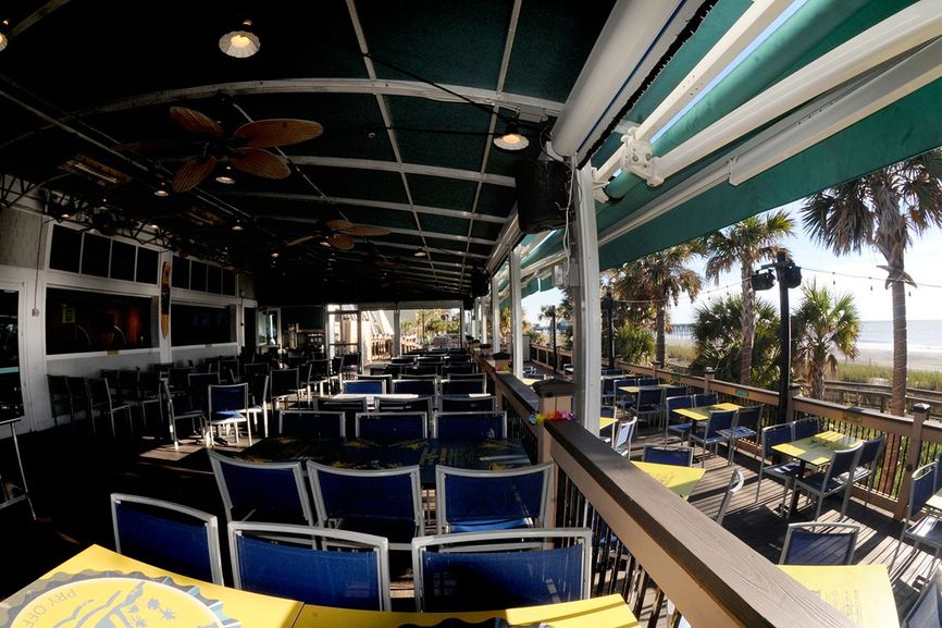 Full venue with indoor and outdoor decks with blue chairs and view on the right of the beach