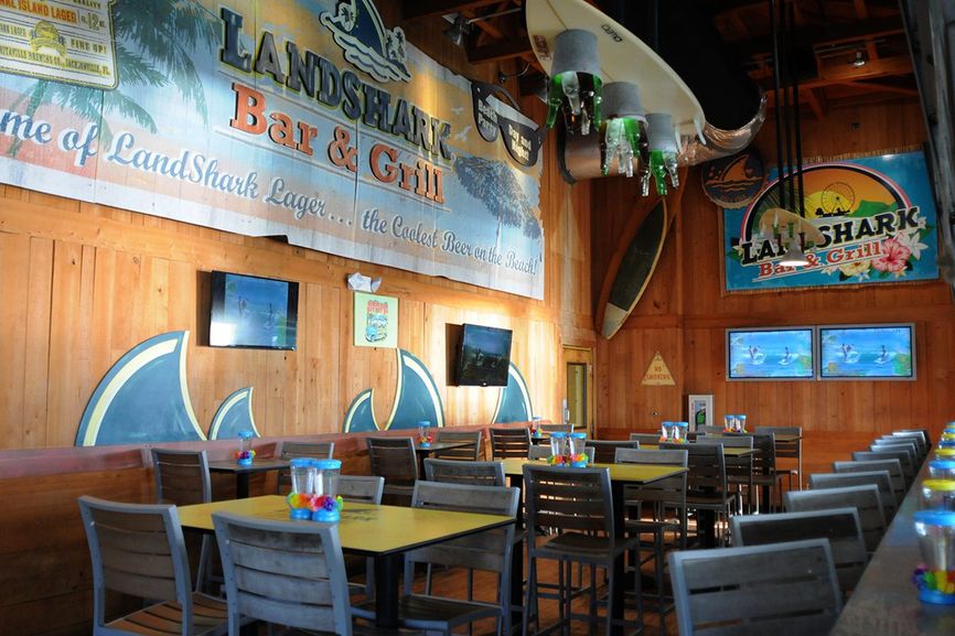 Inside dining with tables and the back of bar stools with a large Landshark sign above the tables