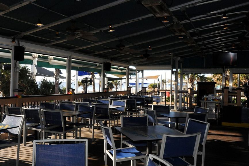 Main deck is enclosed with blue chairs and tables with view of palm trees nad beach in distance