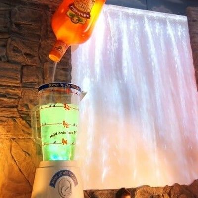 Photo of giant lit-up blender statue pouring drinks in front of a water feature