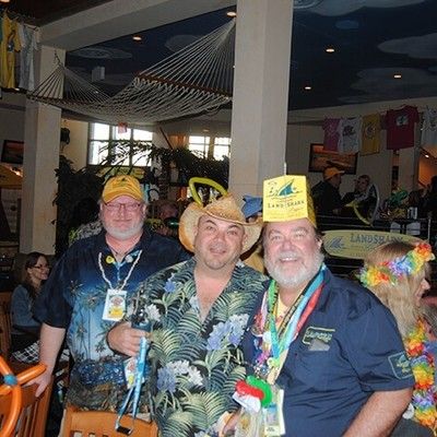 Three men in tropical shirts and party hats posing together