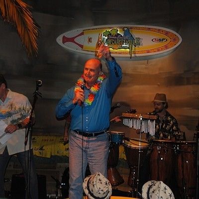 Man wearing a lei singing into a microphone on stage during a party