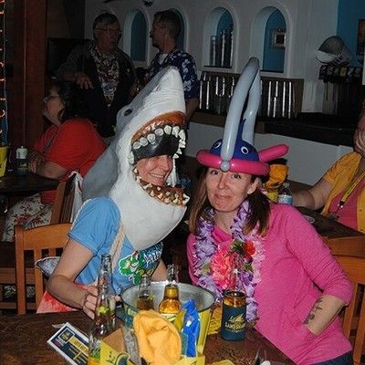 Two women wearing fun plush shark hats and floral leis at a table