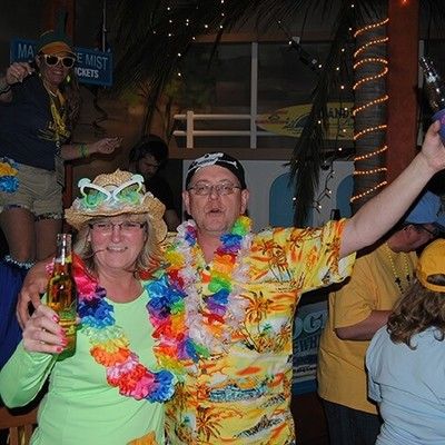 Man and woman wearing hawaiian shirts and leis cheering with beer bottles