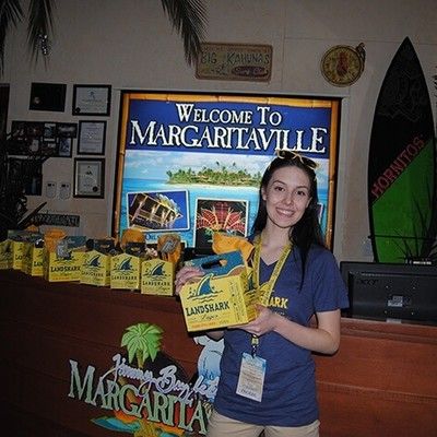 Smiling staff member holding a LandShark pack in front of a Welcome to Margaritaville sign