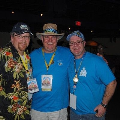 Three men in casual summer attire and hats posing together at an event
