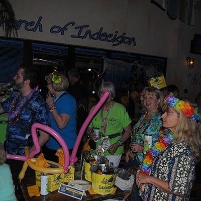 Guests wearing tropical leis and balloon hats enjoying drinks at an indoor event