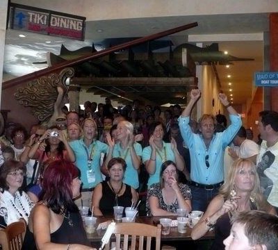 Excited audience and concert fans cheering and taking photos at tables inside the venue