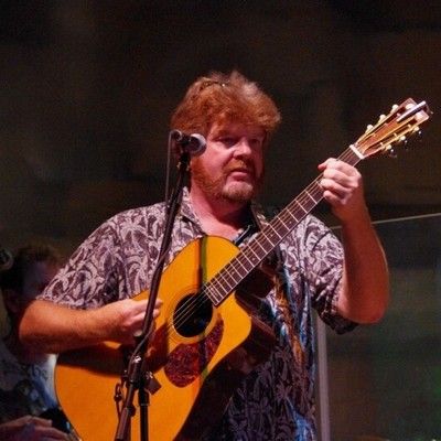 Musician playing acoustic guitar while singing into a microphone on stage
