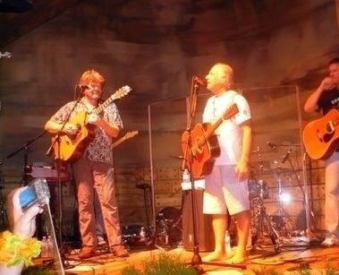 Jimmy Buffett performing live on stage playing acoustic guitar with his band