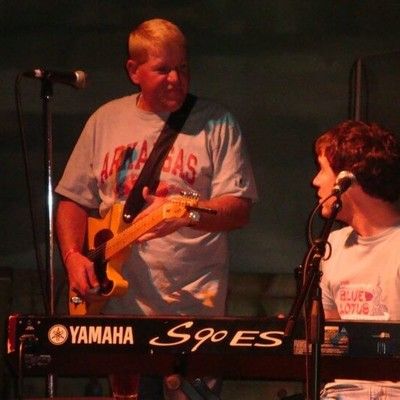 Musician playing electric guitar on stage next to a Yamaha keyboard