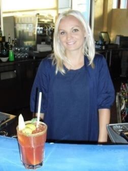 Blonde female bartender posing behind a garnished cocktail at the bar