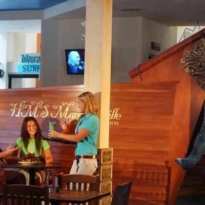 Waitress serving tropical drinks near the HMS Margaritaville wooden boat structure