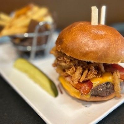 Photo of gourmet cheeseburger with crispy onion straws, served with french fries and a pickle spear