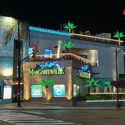 Nighttime exterior view of Margaritaville building illuminated with green neon lights and palm trees