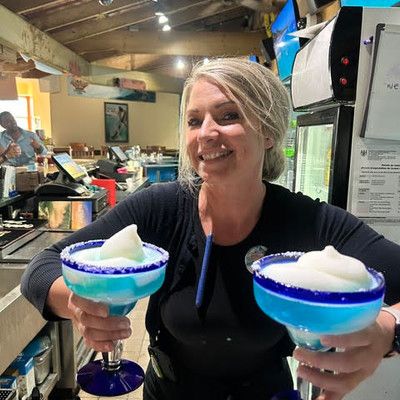 A smiling female staff member presenting two bright blue frozen margaritas