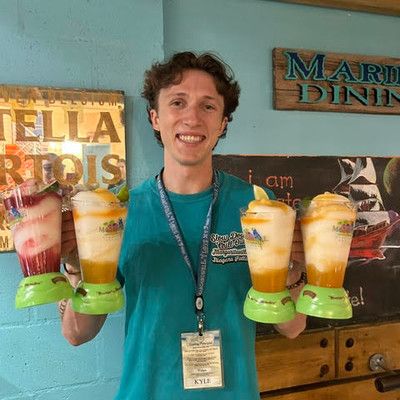 A smiling male server holding up three blended tropical drinks in souvenir blender cups