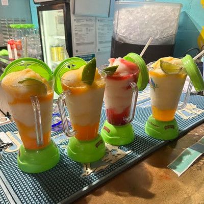 Four colorful blended tropical cocktails lined up in souvenir blender cups on a bar mat