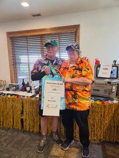 Two participants holding a certificate and prize package at the Parrot Head charity golf tournament