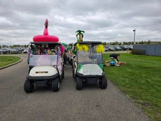Two golf carts decorated with a pink flamingo and palm trees parked outdoors