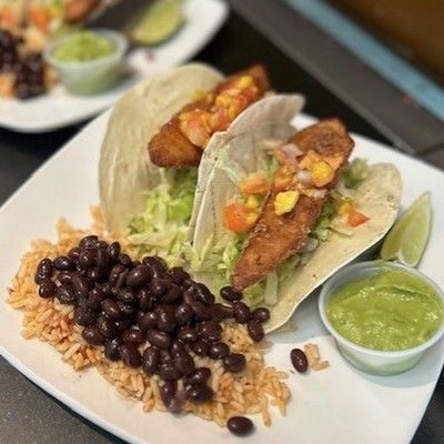 Photo of fish tacos served with black beans, rice, pico de gallo, and guacamole