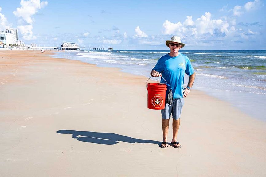 Man holding large buckets on the beach of items collected