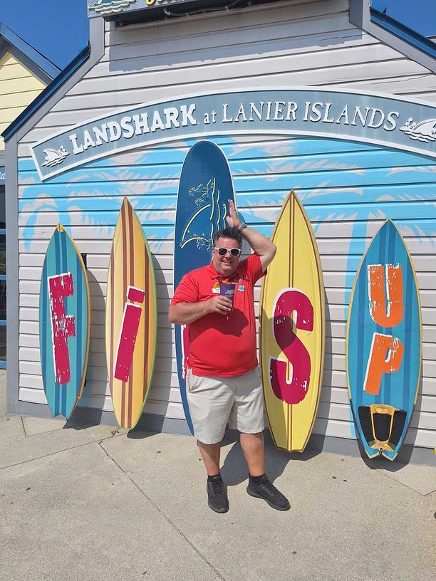 Man making a fins up sign with his hand in front of surfboards that spell out Fins Up