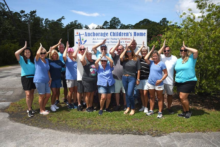 Group of people makign fins up sign with their hands in front of Anchorage Children's Home sign