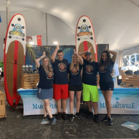 A group of five people in matching promotional t-shirts posing at a Margaritaville event
