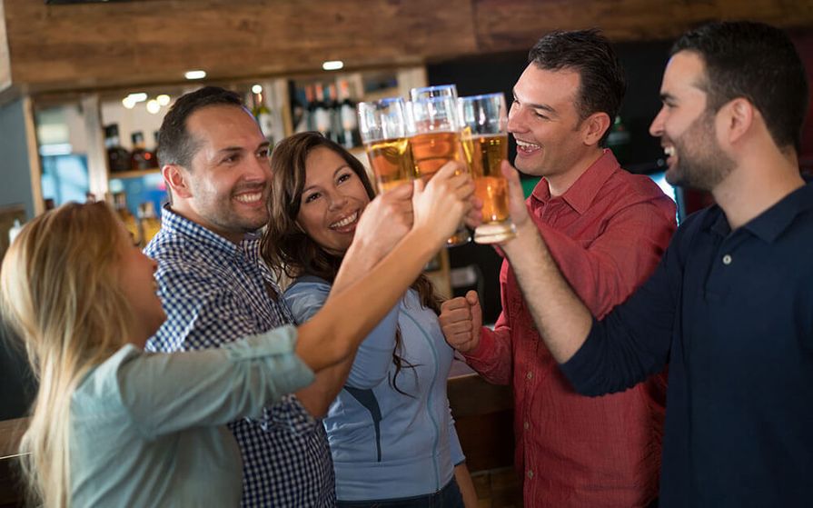 Group of men and women smiling while clinking their beer filled glasses together