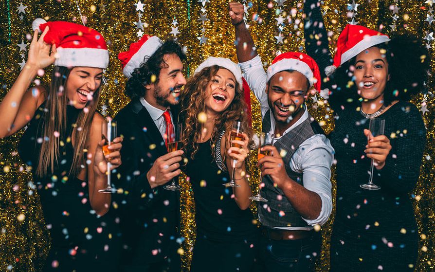 Group of people wearing Santa hats, holding champagne glasses while confetti falls down around them