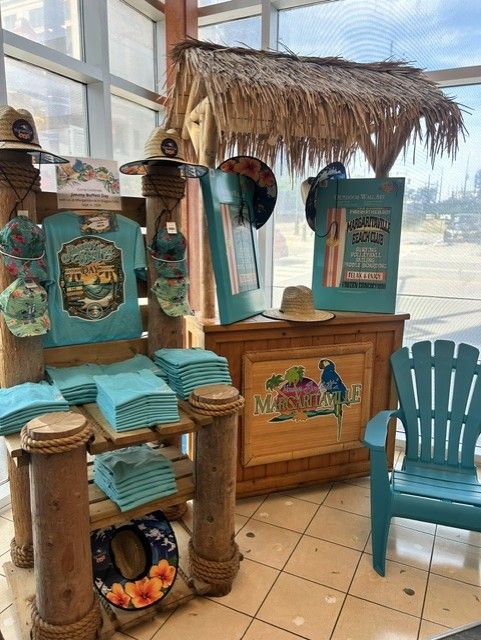 Margaritaville retail display with a thatched hut, teal t-shirts, straw hats, wall art, and a blue beach chair