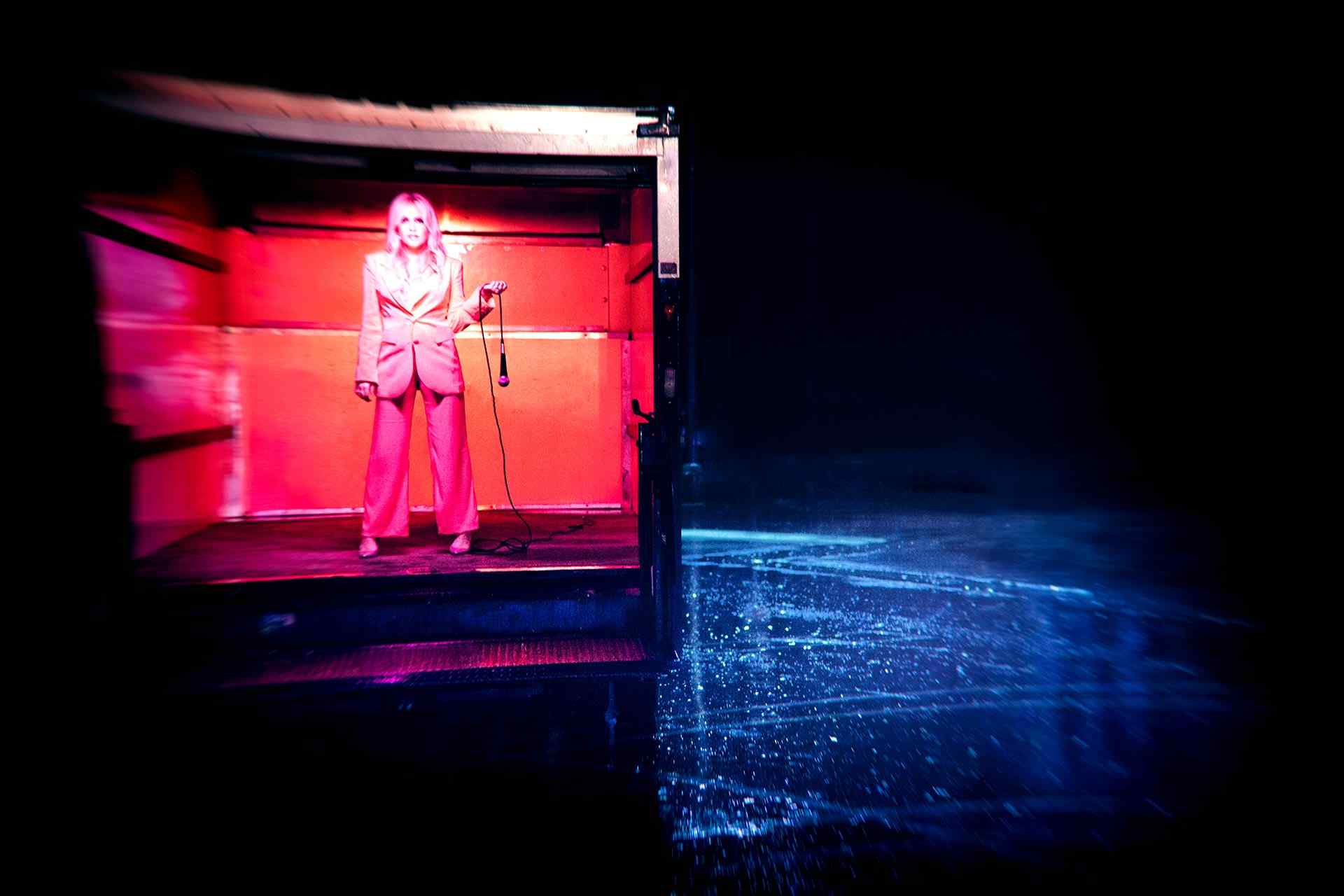 Eden standing in a box truck holding a microphone