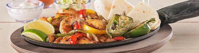 Chicken fajitas on a skillet with lemons and lime, grilled peppers and jalapenos