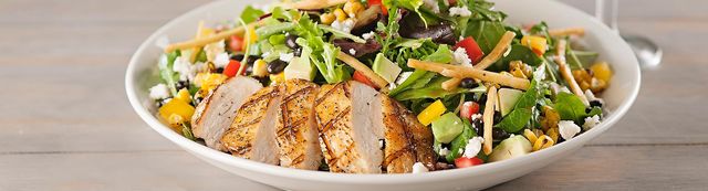 A delicious salad with grilled chicken, lettuce, arugula, corn, cheese and additional toppings